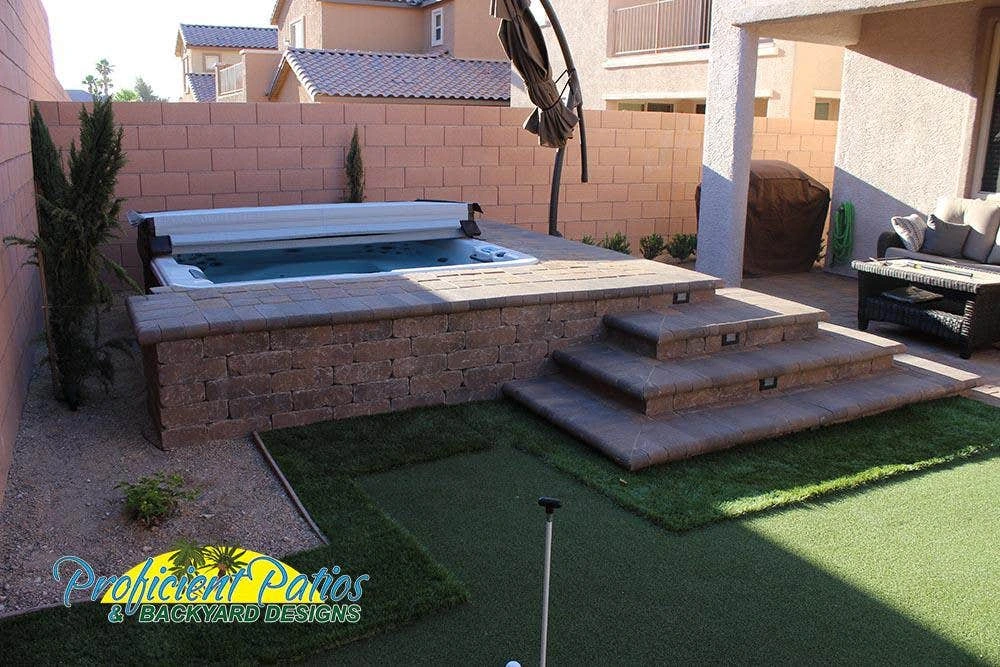 A backyard patio with stone steps, a raised spa, and landscaped pavers in a residential setting.